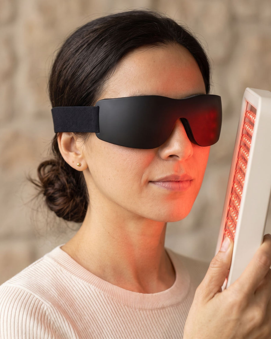 Woman wearing protective goggles, eyes closed, the red-lit Folliq Portable Face Panel about 15 cm from her face