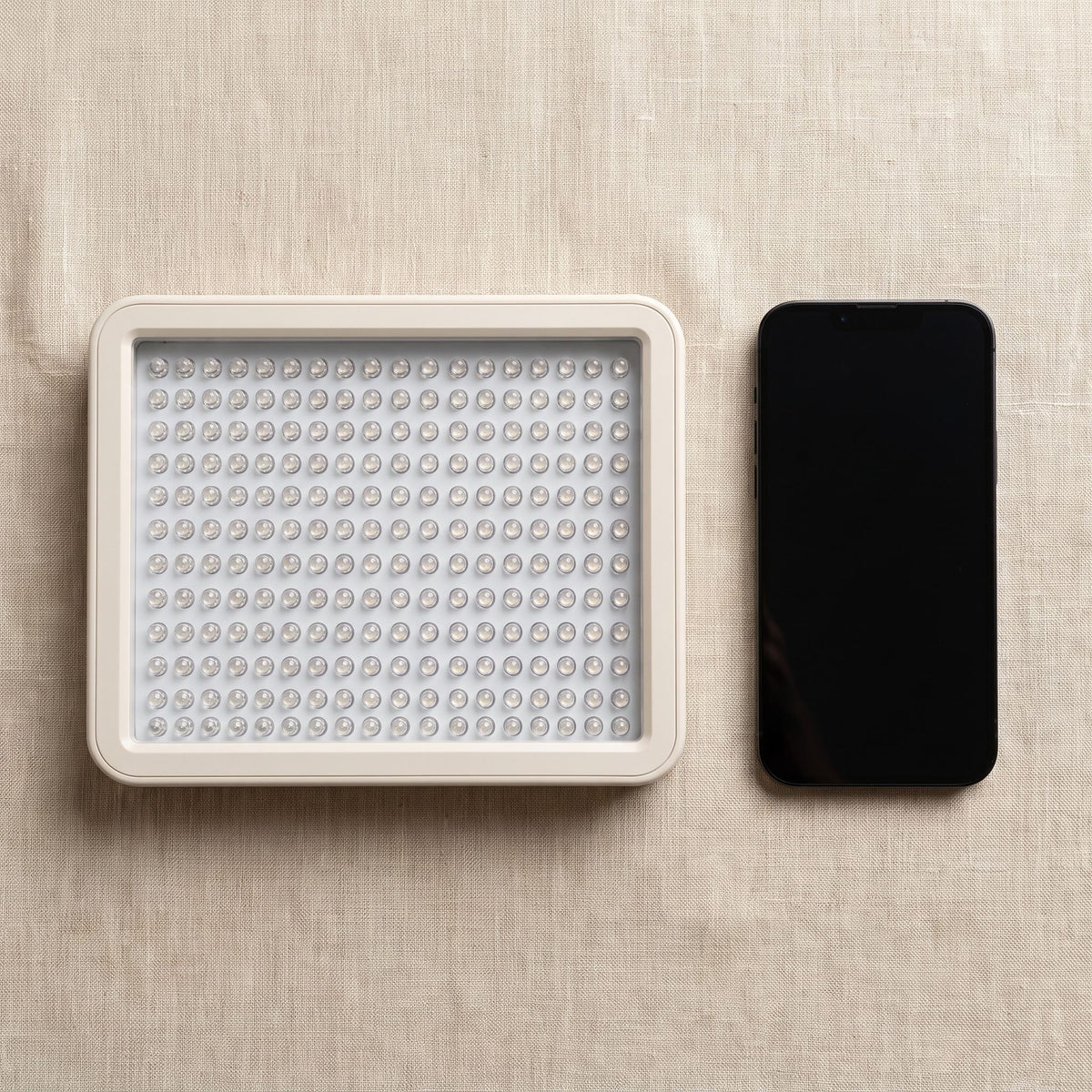 Folliq Portable Face Panel, LEDs off, next to a smartphone, seen from above, for size