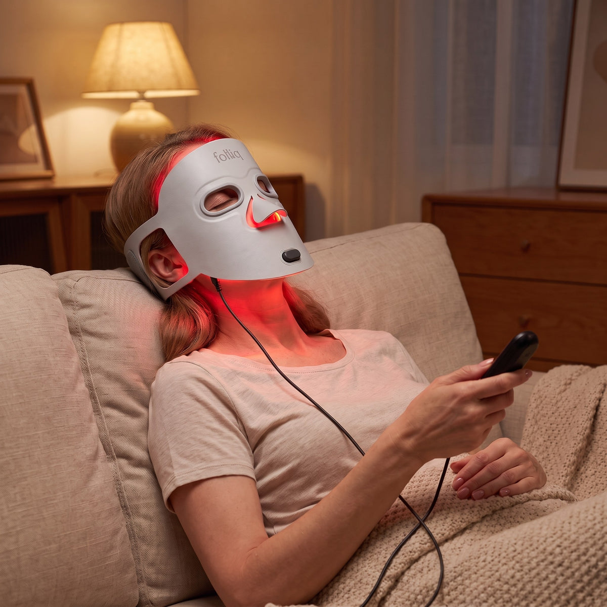 Woman resting on a sofa during a ten-minute session with the Folliq Red Light Therapy Face Mask