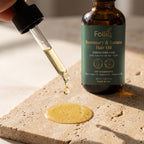 A drop of Folliq Rosemary & Batana Hair Oil falling from the dropper