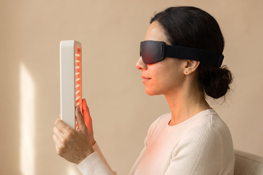 Side view: woman in protective goggles, eyes closed, holding the red-lit panel about 15 cm from her face